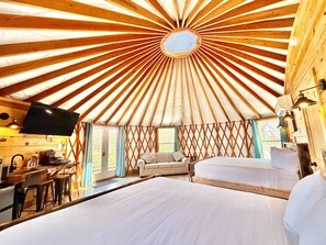 A yurt with a central skylight, a sofa, a bed, and a dining area with a TV and table. - Glamping Yurt near Zion with 2 King Beds & Views (Orderville)