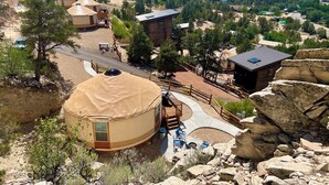A yurt with a covered porch and outdoor seating, surrounded by a rocky landscape and a view of a valley with houses and trees. - Glamping Yurt near Zion with 2 King Beds & Views (Orderville)