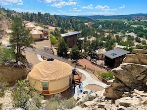 A yurt with a covered porch and outdoor seating, surrounded by a rocky landscape and a view of a valley with houses and trees. - Glamping Yurt near Zion with 2 King Beds & Views (Orderville)