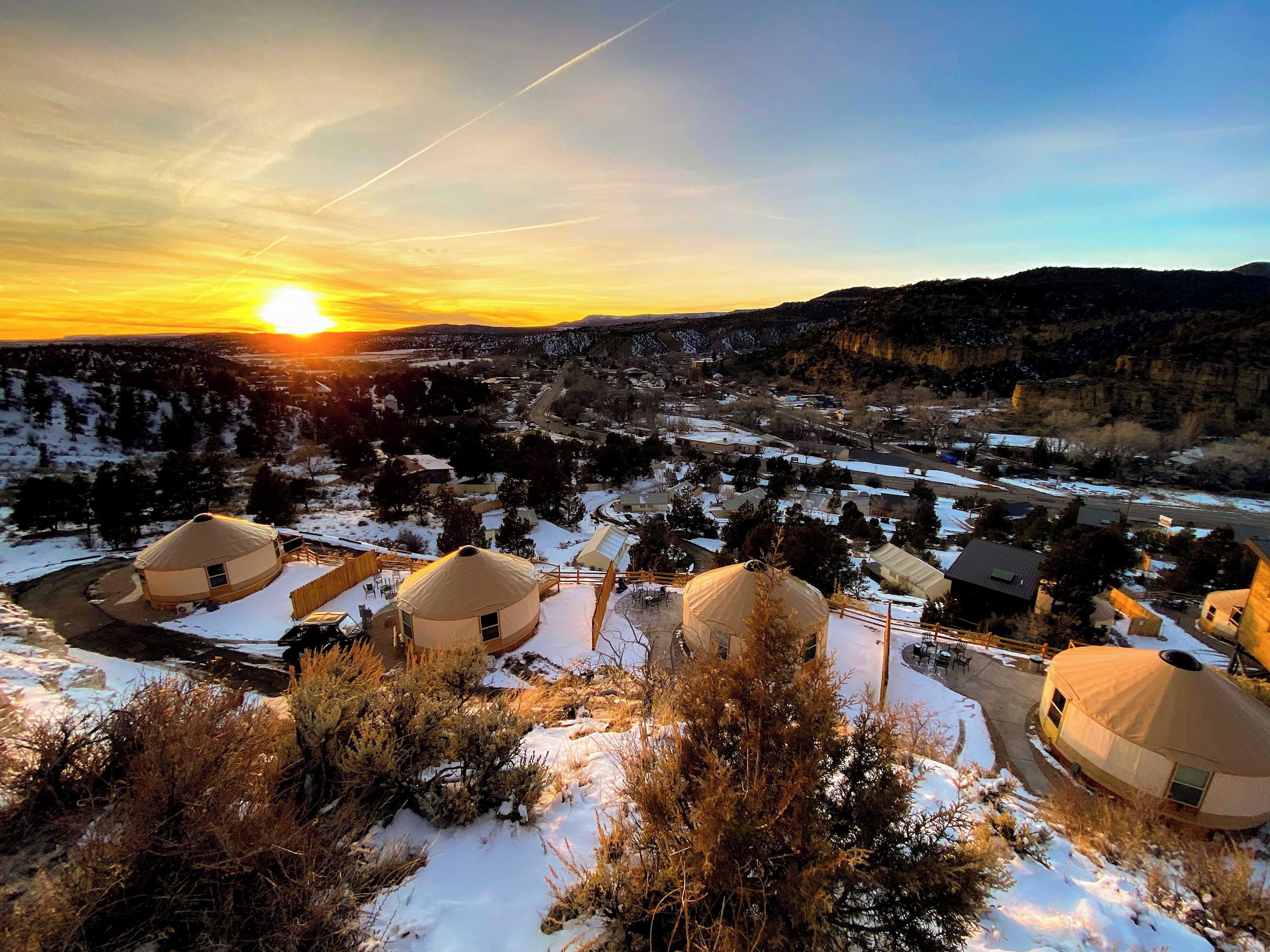 A yurt-style accommodation with a snow-covered landscape and a sunset in the background.