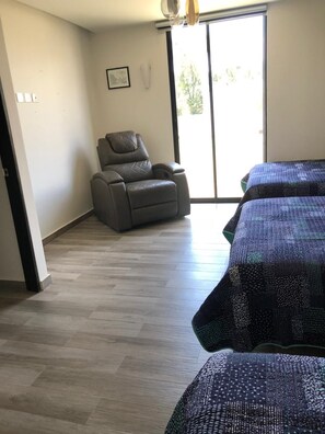 A room with a sliding glass door, a reclining chair, and a bed with a patterned bedspread.