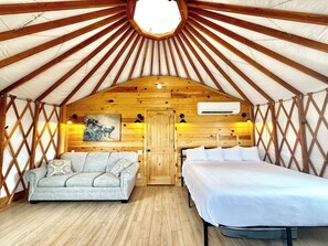 En hyggelig yurt-indretning med træloft, sofa, seng og et billede på væggen.