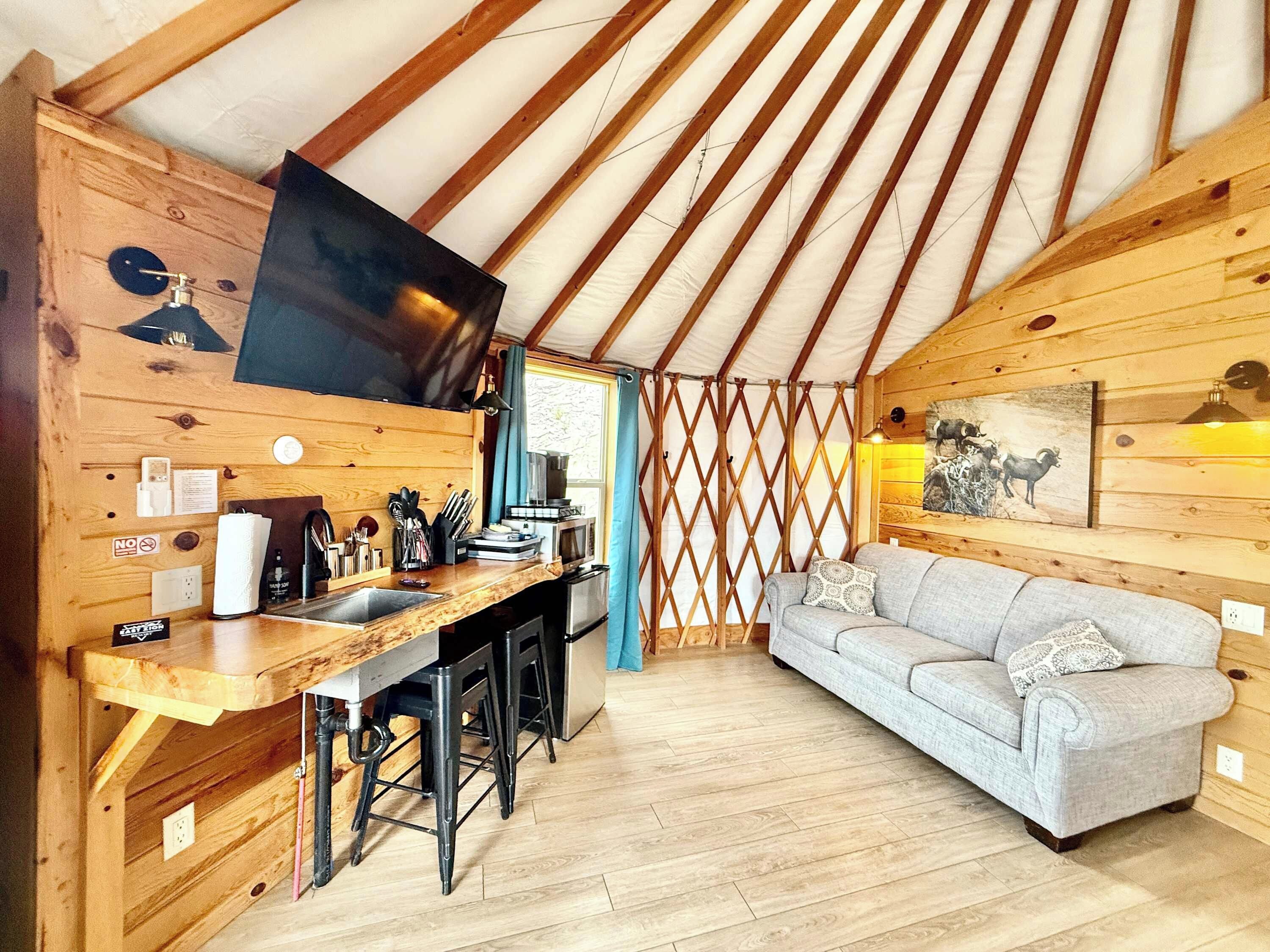 A cozy interior with a wooden kitchen, a sofa, and a TV mounted on the wall.