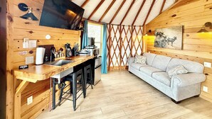En ombonad inredning med ett kök i trä, en soffa och en tv som är monterad på väggen.