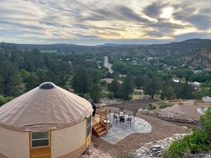 Eine Jurte mit einer Holzterrasse und Sitzgelegenheit im Freien, umgeben von einer gebirgigen Landschaft.