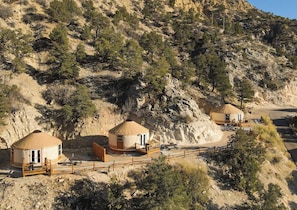Un alloggio in stile yurta con terrazza in legno, immerso in un paesaggio naturale caratterizzato da vegetazione rada e terreno roccioso.