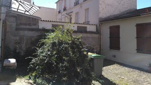 A courtyard with a tree, a covered area, and buildings with balconies and windows. - Comfortable & affordable Parisian studio near the metro. (Ivry-sur-Seine)