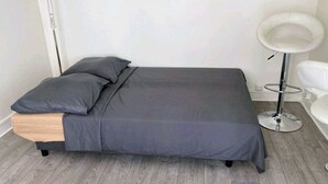 A single bed with a wooden headboard, grey bedding, and a white round side table with a stool. - Comfortable & affordable Parisian studio near the metro. (Ivry-sur-Seine)