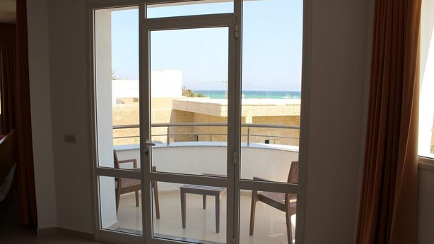 Quarto com porta de correr de vidro que dá para uma varanda com vista para o mar e edifícios.