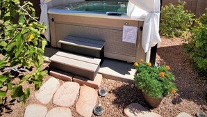 Un jacuzzi con toldo, rodeado de escalones de piedra y plantas en macetas.