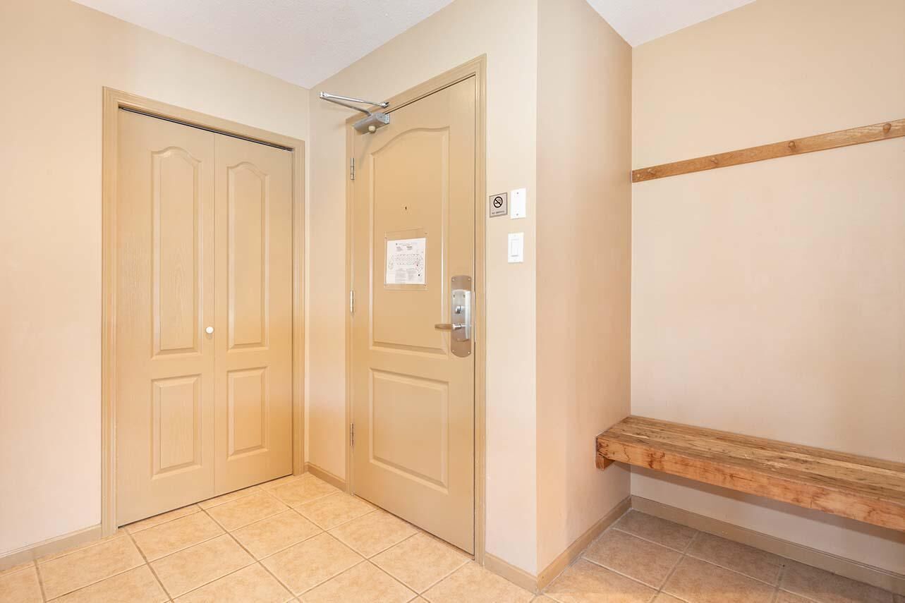 A hallway with two doors, a bench, and a wall-mounted shelf.