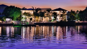 Ein Hotel am Wasser mit Pool, Palmen und einem Sonnenuntergang.