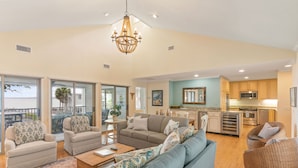 A spacious living area with a large sofa, a coffee table, and a dining table. There is a kitchen area with modern appliances and a balcony with a view. - Direct Ocean Front, Private Pool, 100 steps to Lighthouse (St Simons Island)