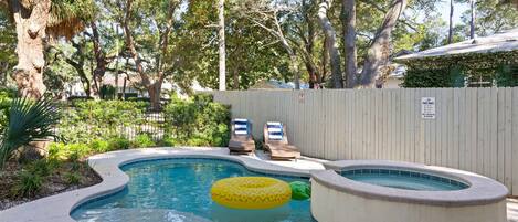 A swimming pool with a hot tub, lounge chairs, and a wooden fence.
