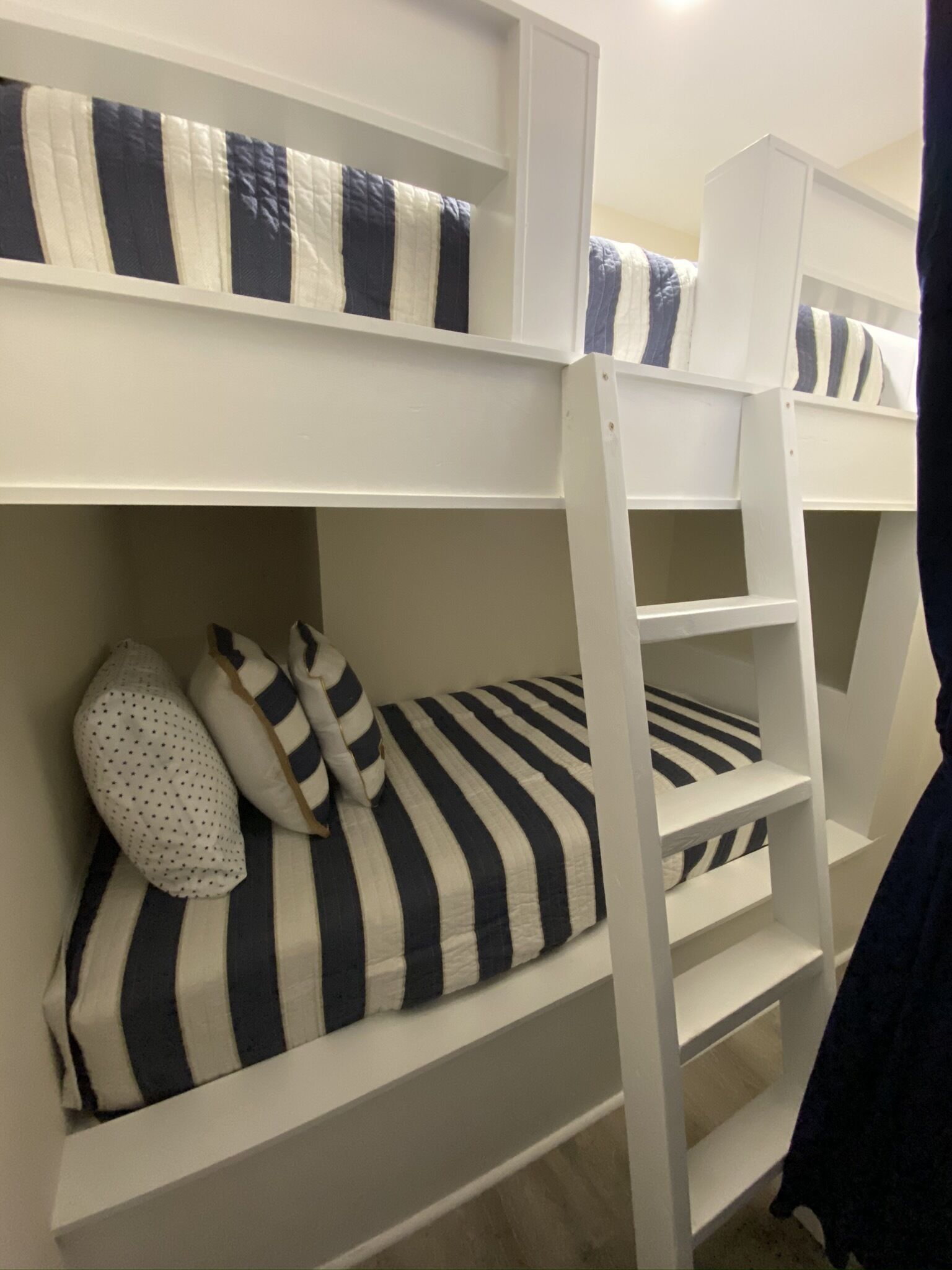 A bunk bed with striped bedding and pillows, white walls, and a ladder.