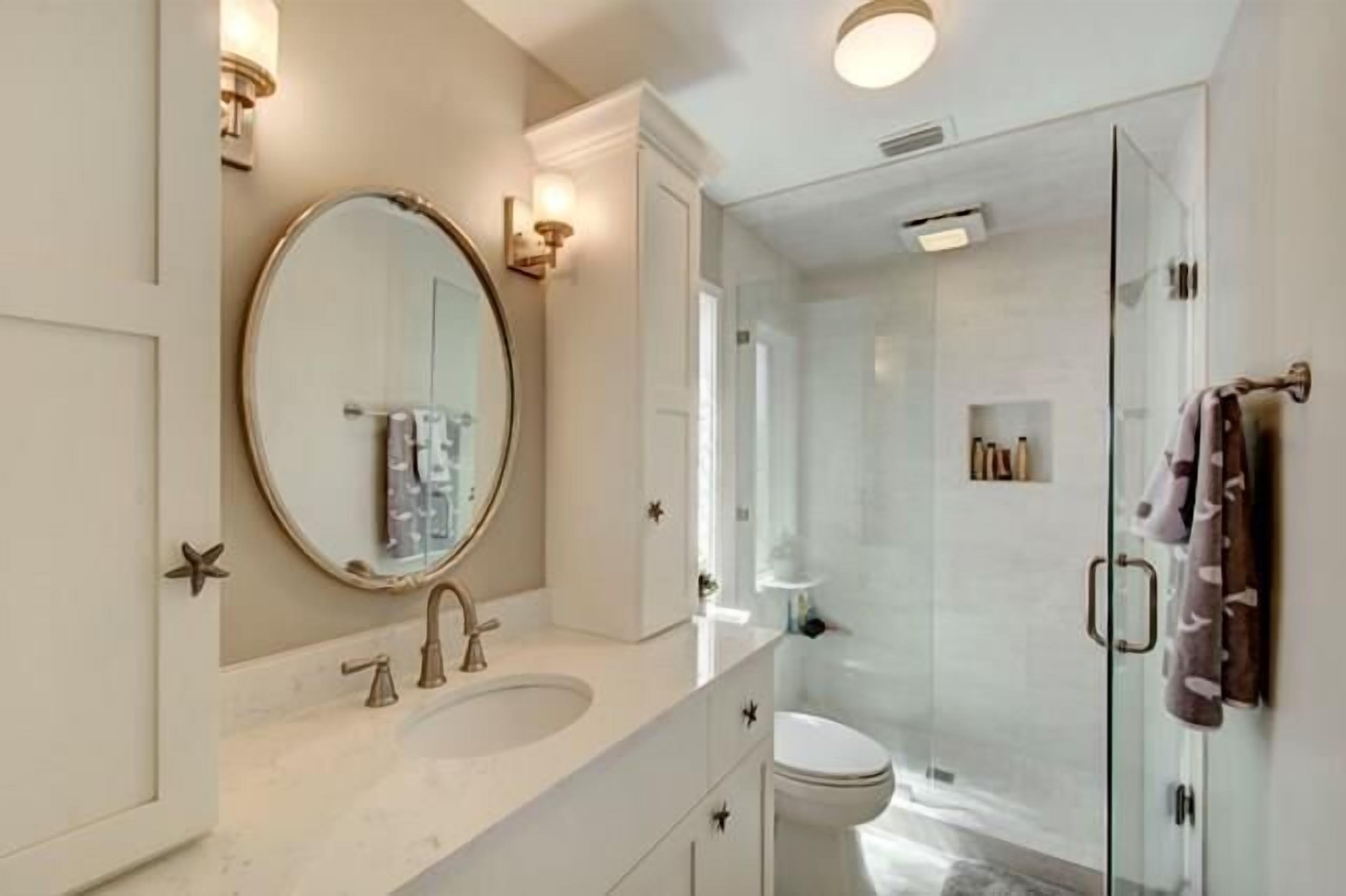 A modern bathroom with a round mirror, a sink, and a glass-enclosed shower.