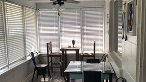 A dining area with a table and chairs, a ceiling fan, and large windows with blinds.