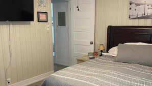 A bedroom with a bed, a ceiling fan, a television, and a door leading to another room.