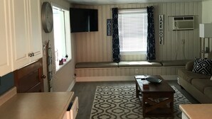 A compact living space with a kitchenette, a seating area with a bench, and a window with blinds.