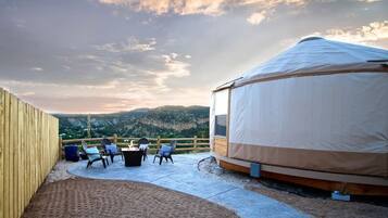 A yurt with a covered outdoor seating area and a view of mountains.
