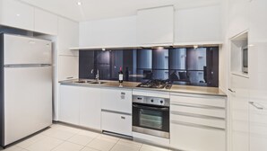 A modern kitchen with white cabinetry, a stainless steel refrigerator, a built-in oven, and a gas stove. - Circle on Cavill Ocean View (Surfers Paradise)