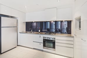 A modern kitchen with white cabinetry, a stainless steel refrigerator, a built-in oven, and a gas stove. - Circle on Cavill Ocean View (Surfers Paradise)