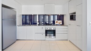 A modern kitchen with white cabinetry, stainless steel appliances, and a built-in oven. - Circle on Cavill Ocean View (Surfers Paradise)