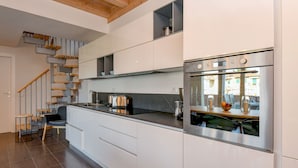 Eine moderne Küche mit weißen Schränken, einem Edelstahlbackofen und einem eingebauten Kochfeld. Es gibt eine Treppe mit Holzsitzstufen und einen Stuhl.
