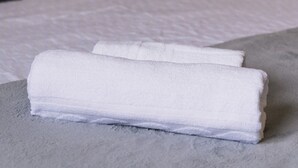 Ein ordentlich bezogenes Bett mit Kissen und einem gefalteten Handtuch auf einer strukturierten Oberfläche.