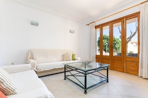Ein Wohnzimmer mit Glastisch, beiger Couch und Holztür mit Glaseinsätzen.