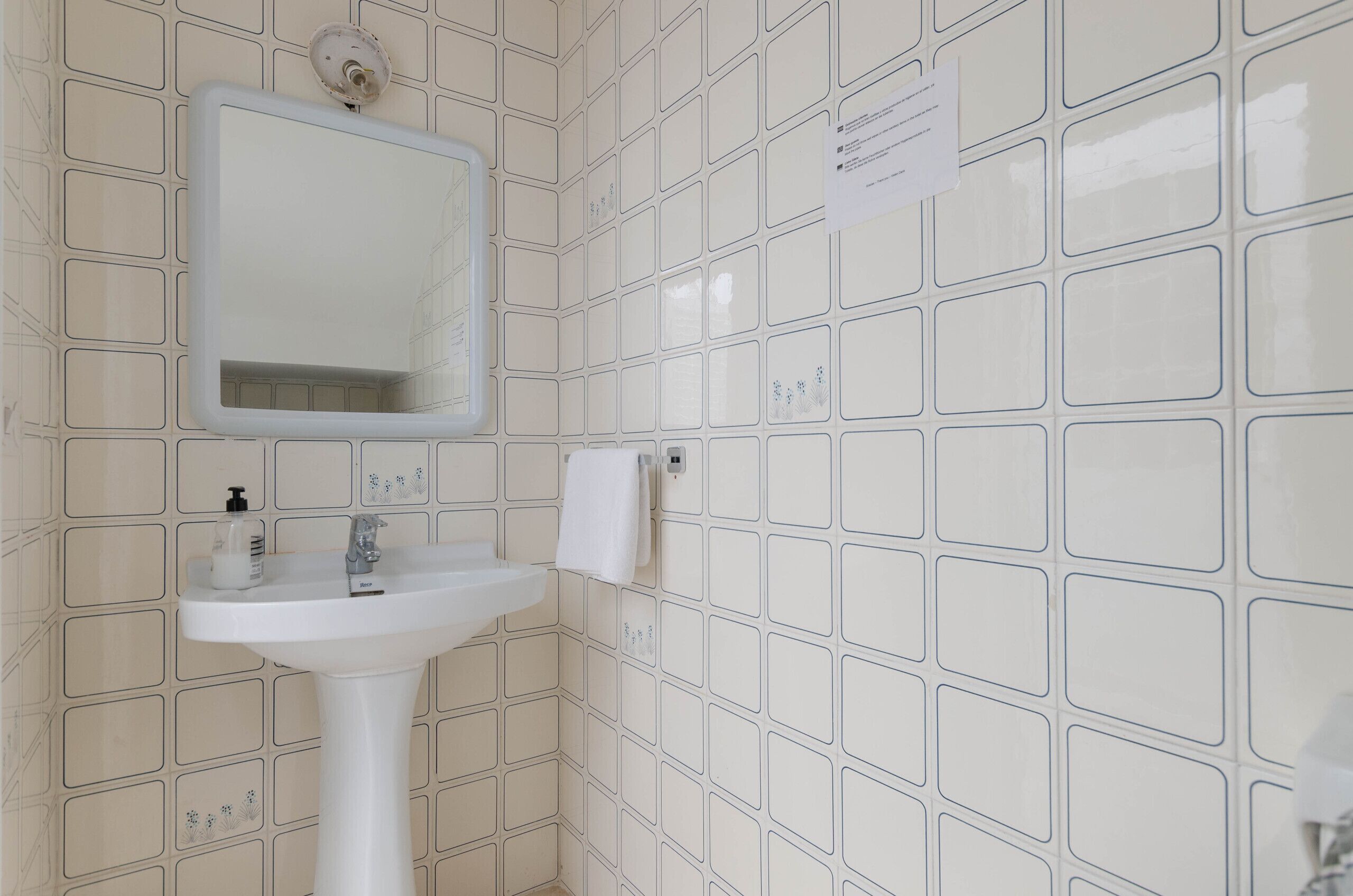 Une salle de bain avec un lavabo blanc, un miroir et des murs carrelés.