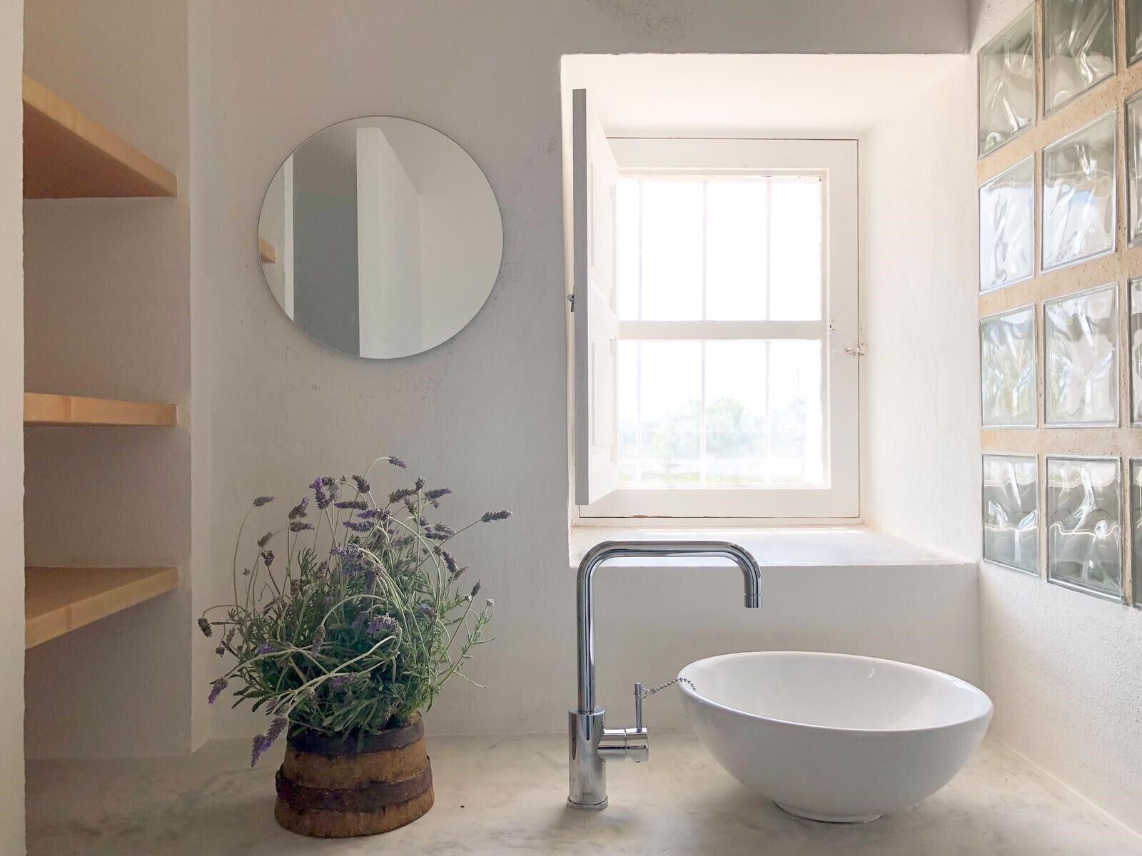 A bathroom with a white sink, a round mirror, and a window with frosted glass panels.