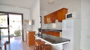 Una cocina con armarios de madera, un refrigerador blanco, microondas, cafetera e isla de vidrio con taburetes.