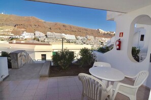 A balcony with a view of a mountainous landscape, white outdoor furniture, and a fire extinguisher on the wall. - Comfortable Apartment in Puerto Rico (Mogán)