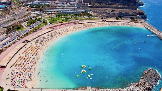 Un complejo turístico costero con una extensa playa de arena, una zona para nadar y un acantilado rocoso.