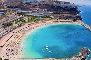 Ein Küstenort mit einem breiten Sandstrand, einem Schwimmbereich und einer felsigen Klippe.