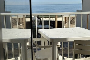 Un balcó amb caires de plàstic blanc i taules, amb vista a una platja i al mar.