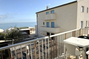 Un balcone con vista sul mare, un tavolo bianco e una sedia.