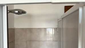 Um chuveiro com chuveiro cromado, paredes azulejadas e teto branco.