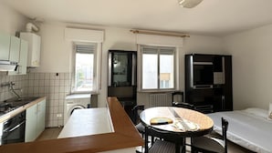 Cozinha compacta com máquina de lavar, mesa de jantar com cadeiras e uma cama.