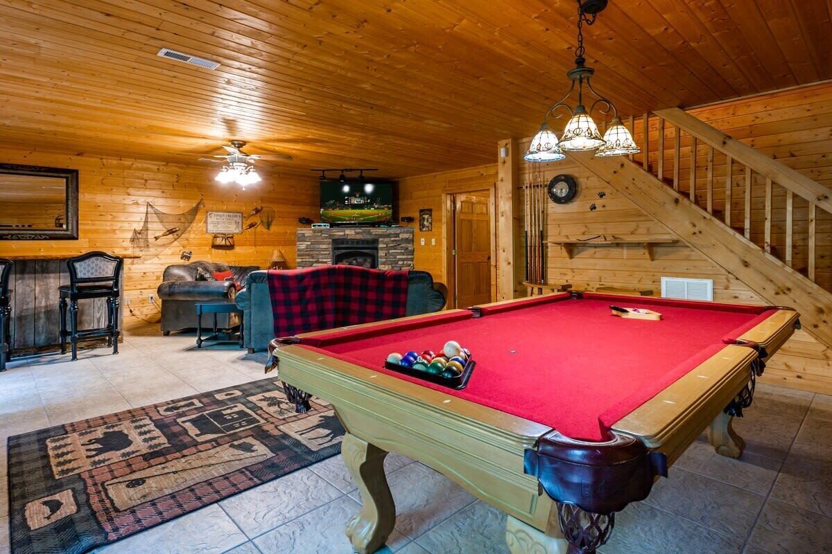 Ein Billardtisch in einem Holzraum mit Kamin, Fernseher und Treppe.