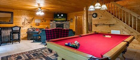 Ein Billardtisch in einem Holzraum mit Kamin, Fernseher und Treppe.