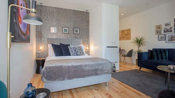 Ett modernt sovrum med en stor säng, ett sängbord, en lampa och en mörkblå soffa i en samtida miljö.