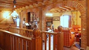 A rustic wooden interior with a loft area, a fireplace, and a cozy seating area with plaid cushions.