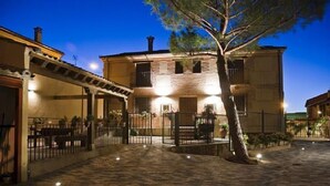A courtyard with a stone-paved ground, a central tree, and a building with a stone facade and multiple windows.