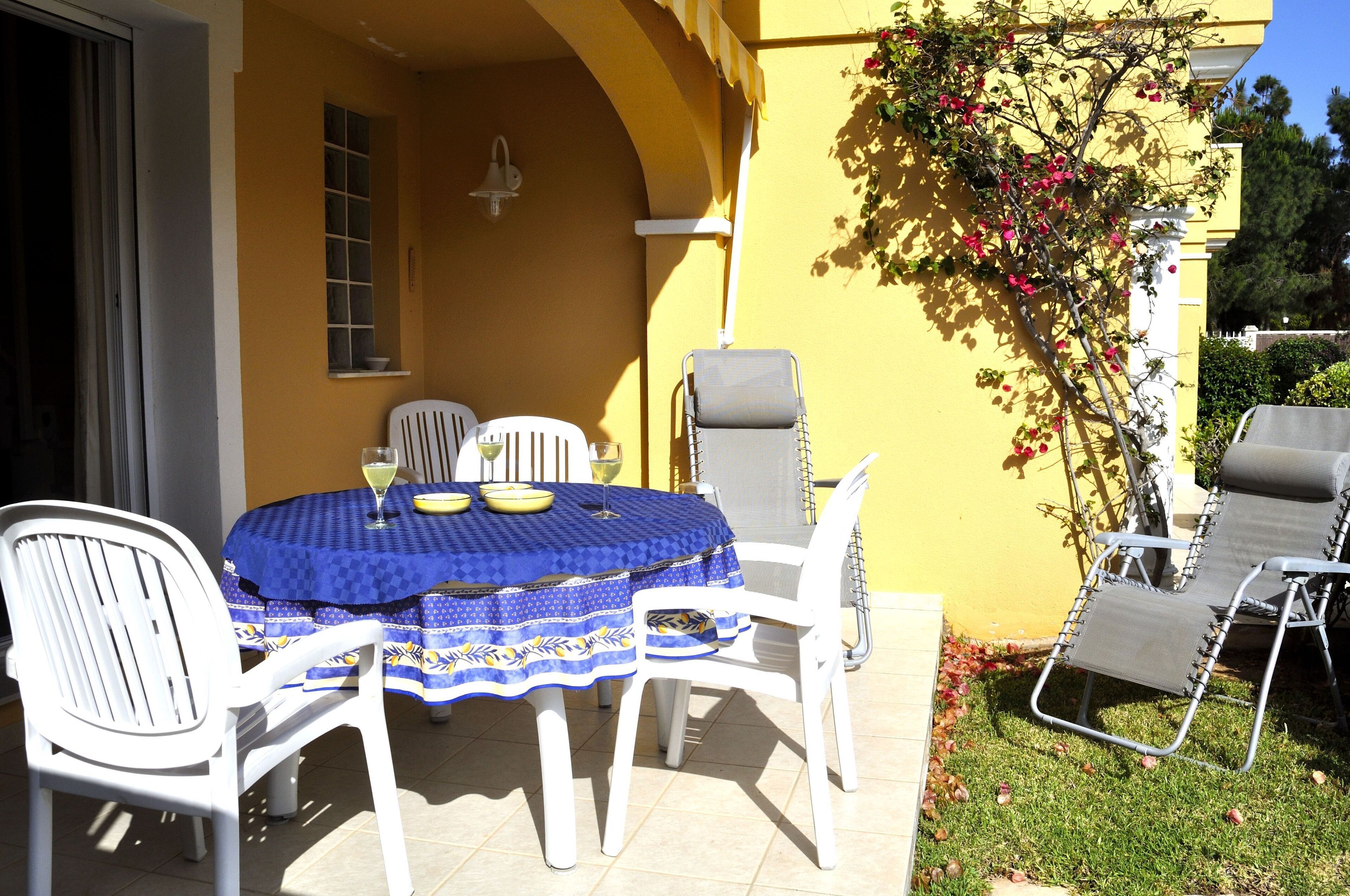 A patio with a round table, white chairs, and a blue tablecloth.
