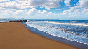 A beach with a wide sandy shore, waves gently lapping at the edge, and a clear blue sky with scattered clouds. - aldeamar, bungalow - 2 bedrooms in quiet urbanization. (Els Poblets)