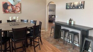 Un coin repas avec une table ronde, des chaises et un luminaire suspendu. On y trouve également un bar avec des tabourets et un tableau représentant un paysage urbain accroché au mur.