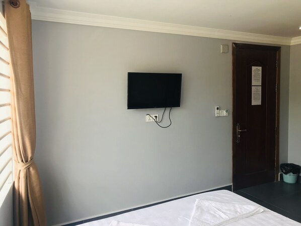 A hotel room with a bed, a television mounted on the wall, a door with a notice, and a trash bin. - Maison Rivera Guest House (Kampot)