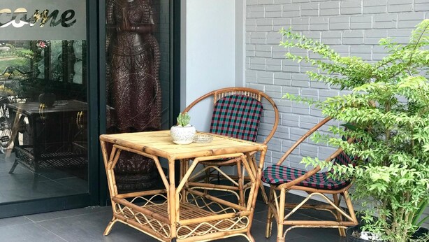 A wicker table and chairs outside a building with a large statue and a sign. - Maison Rivera Guest House (Kampot)